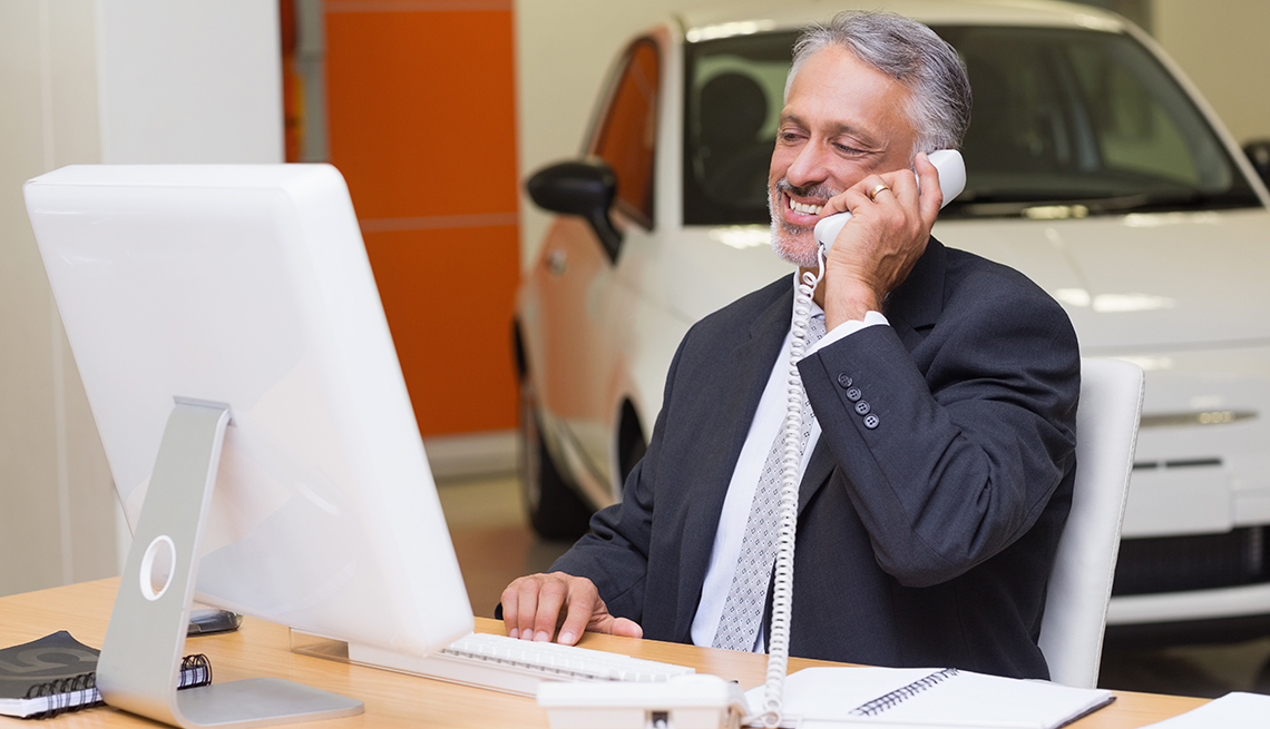 Smiling businessman using laptop on the phone at new car showroom
